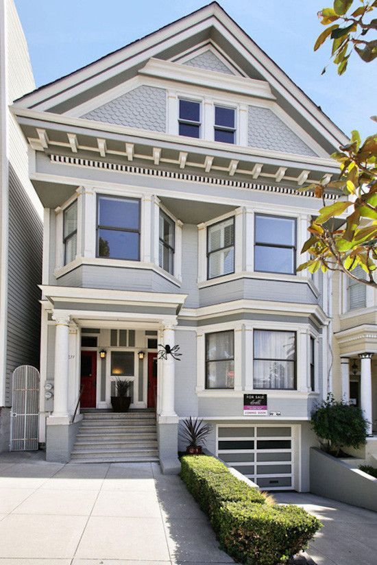 Gray Victorian-style house with bay windows, steps, and a garage door, on a city street.