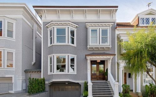 Gray house with white trim, bay windows, and a brown front door.