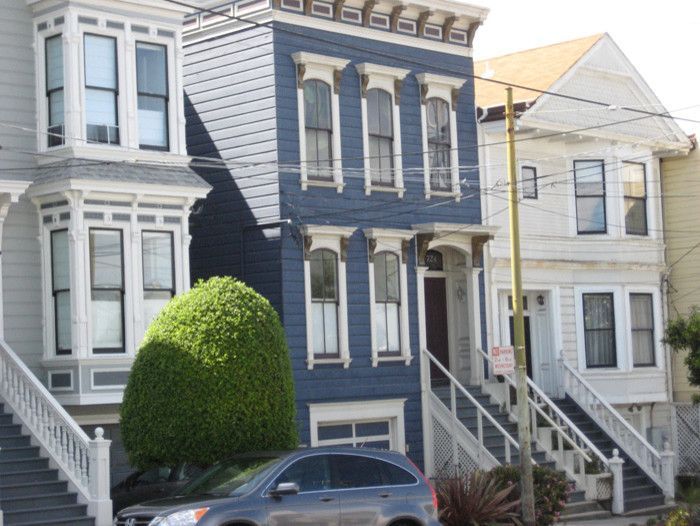 Row of colorful Victorian houses with stairs and car.