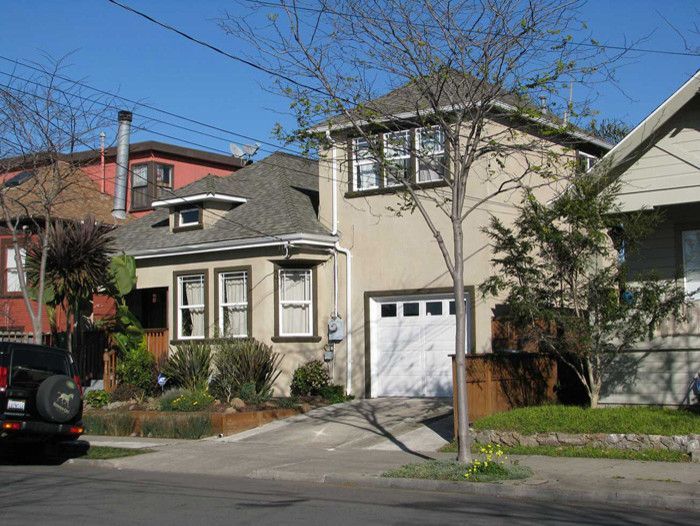Tan two-story house with attached garage, driveway, and small garden in front.