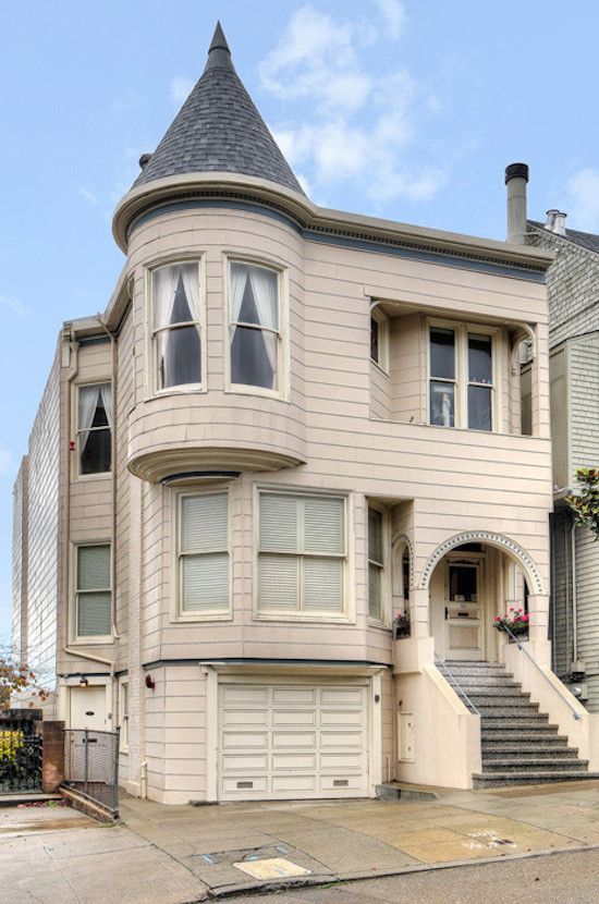 Beige three-story house with turret, arched entrance, and garage door. Steps lead up to the front door.
