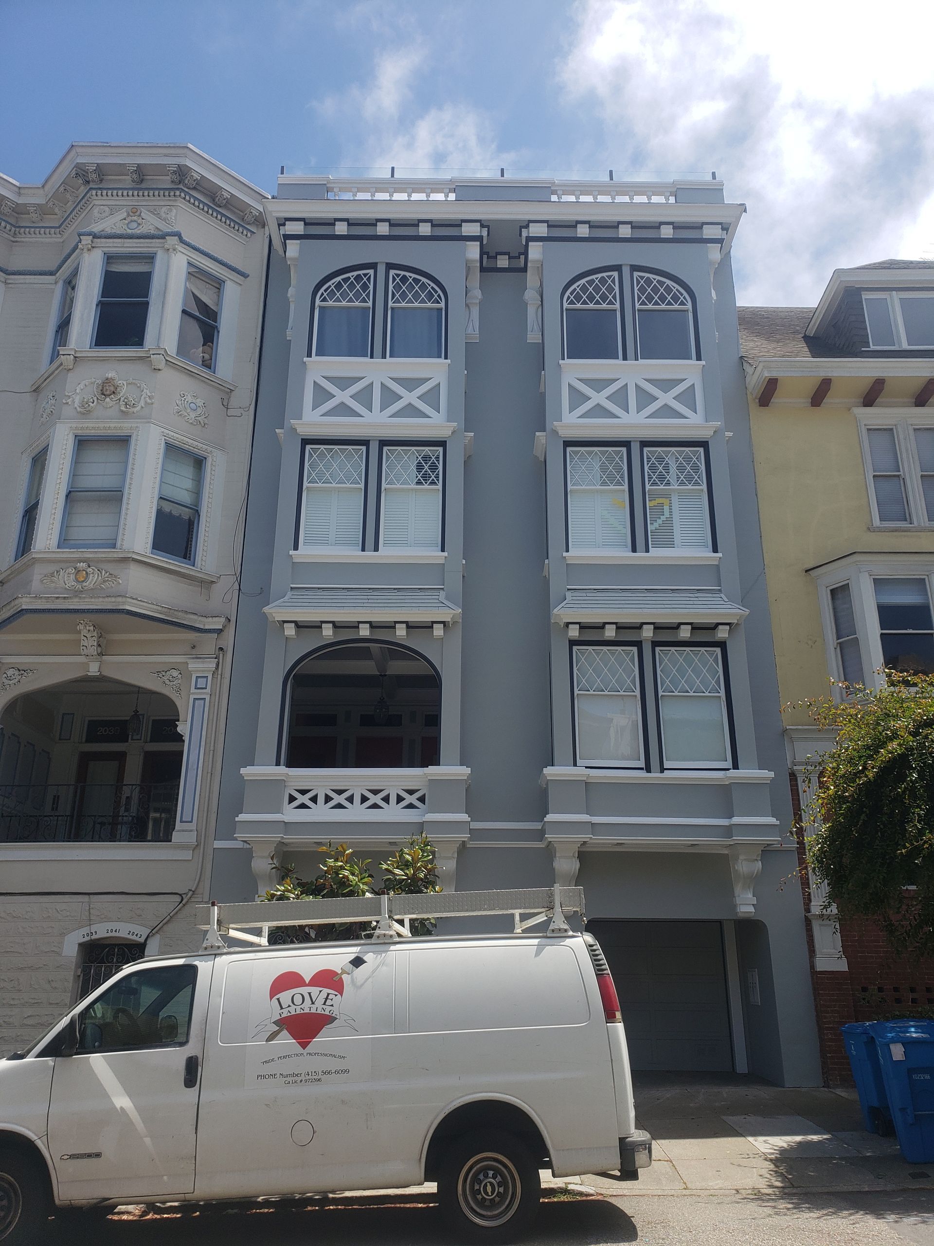 A tall, light-blue apartment building with white trim, a garage, and a white van parked in front.