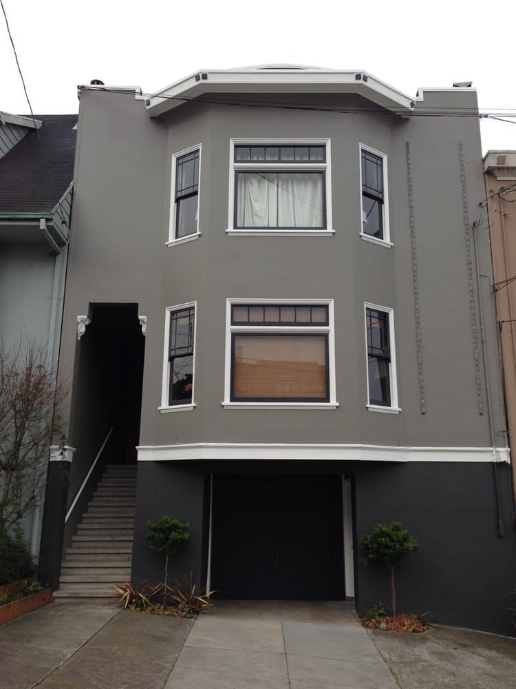 Gray multi-story building with a garage, bay windows, and a staircase leading to the entrance.