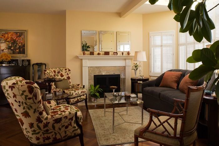 Cozy living room with floral chairs, dark sofa, fireplace, mirrors, and a plant.