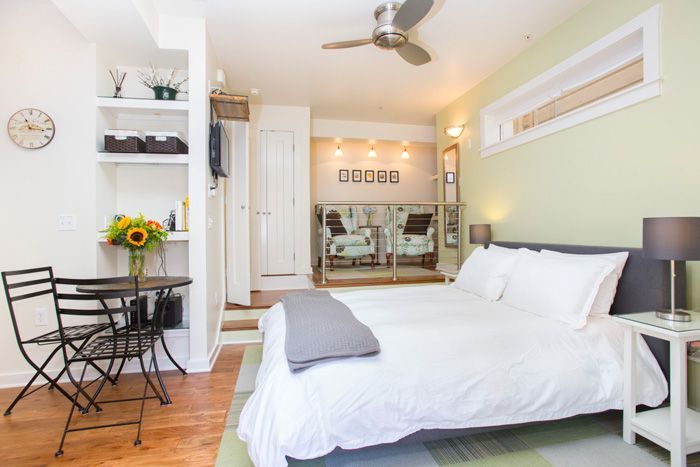 Cozy studio apartment with a bed, small table, and shelves; light green wall.