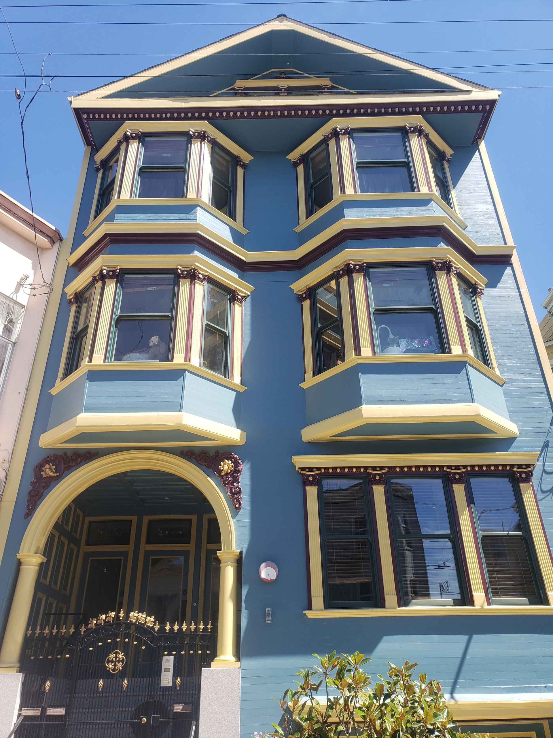 Blue Victorian building with bay windows, ornate trim, and wrought iron gate.