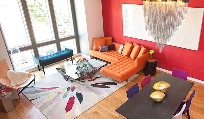 Living room with orange sectional, red wall, colorful rug, and chandelier.
