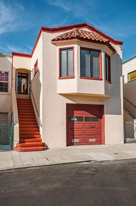 Two-story stucco house with red trim, bay window, and garage door. Exterior stairs lead to the front door.
