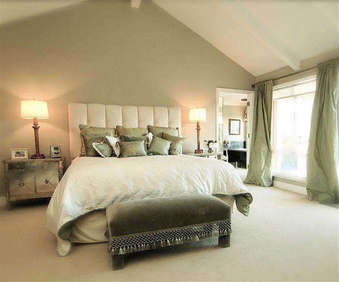 Bedroom with a tall headboard, sage green accents, and white linens. Features lamps, nightstand, and curtains.
