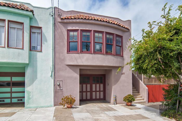 Two-story stucco house, light purple exterior with garage door. Green house to the left and red door/stairs to the right.