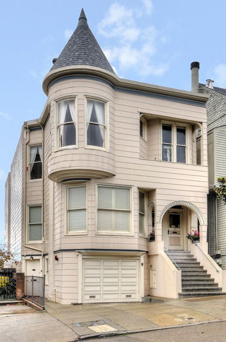 Beige Victorian house with turret, arched entrance, and garage. Gray roof, steps to front door.