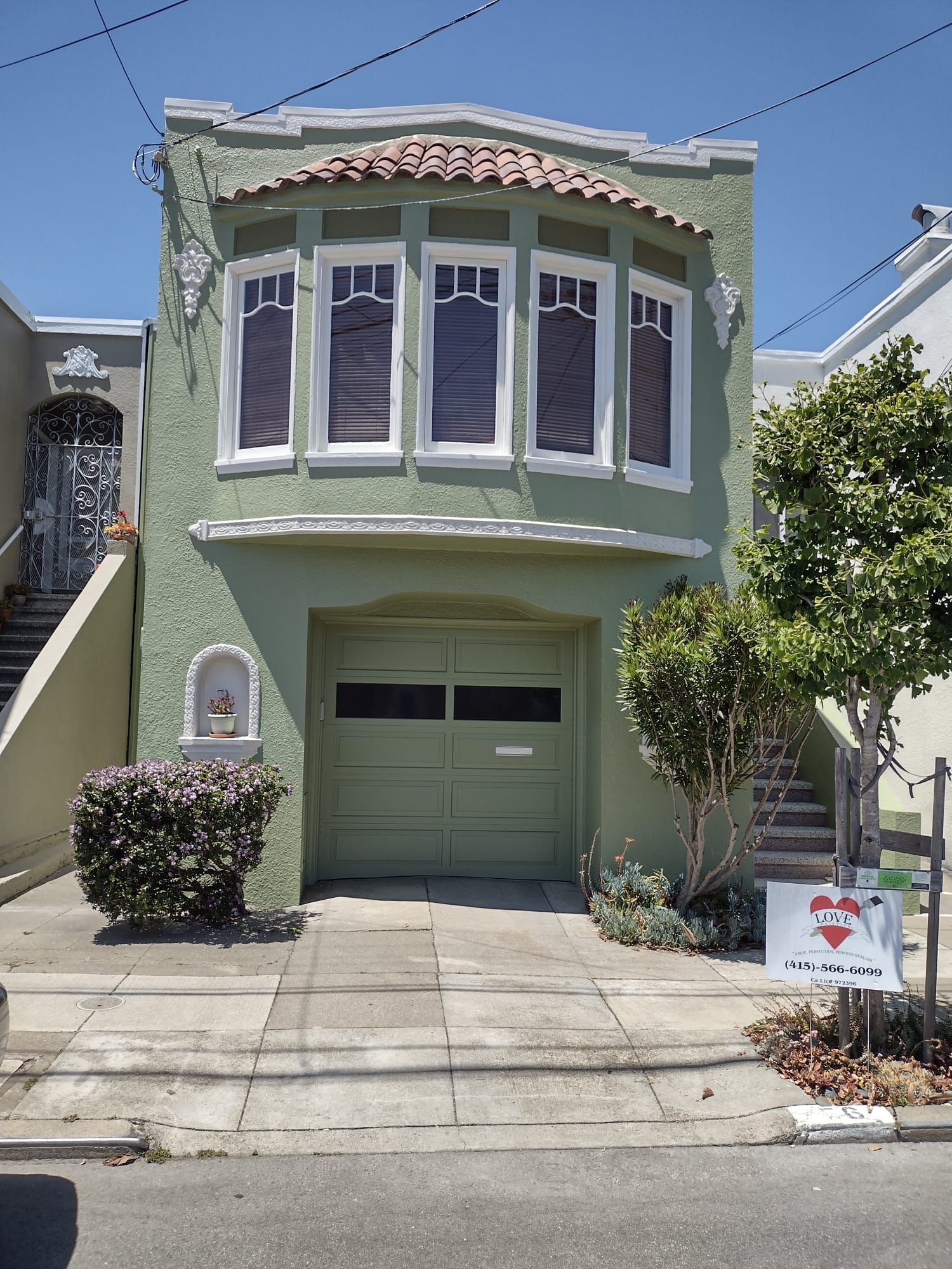 Green stucco two-story house with arched windows and a garage door. Small garden in front.