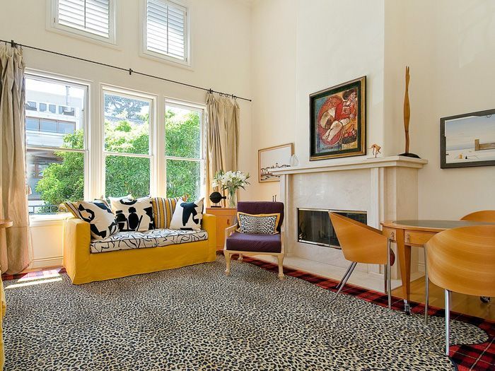 Living room with a yellow couch, fireplace, large windows, and patterned rug.