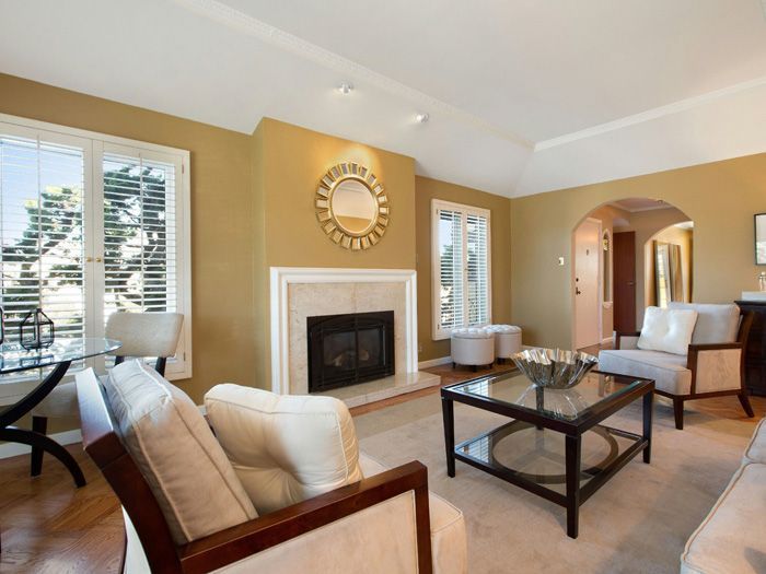 Living room with fireplace, gold walls, white furniture, and large windows.