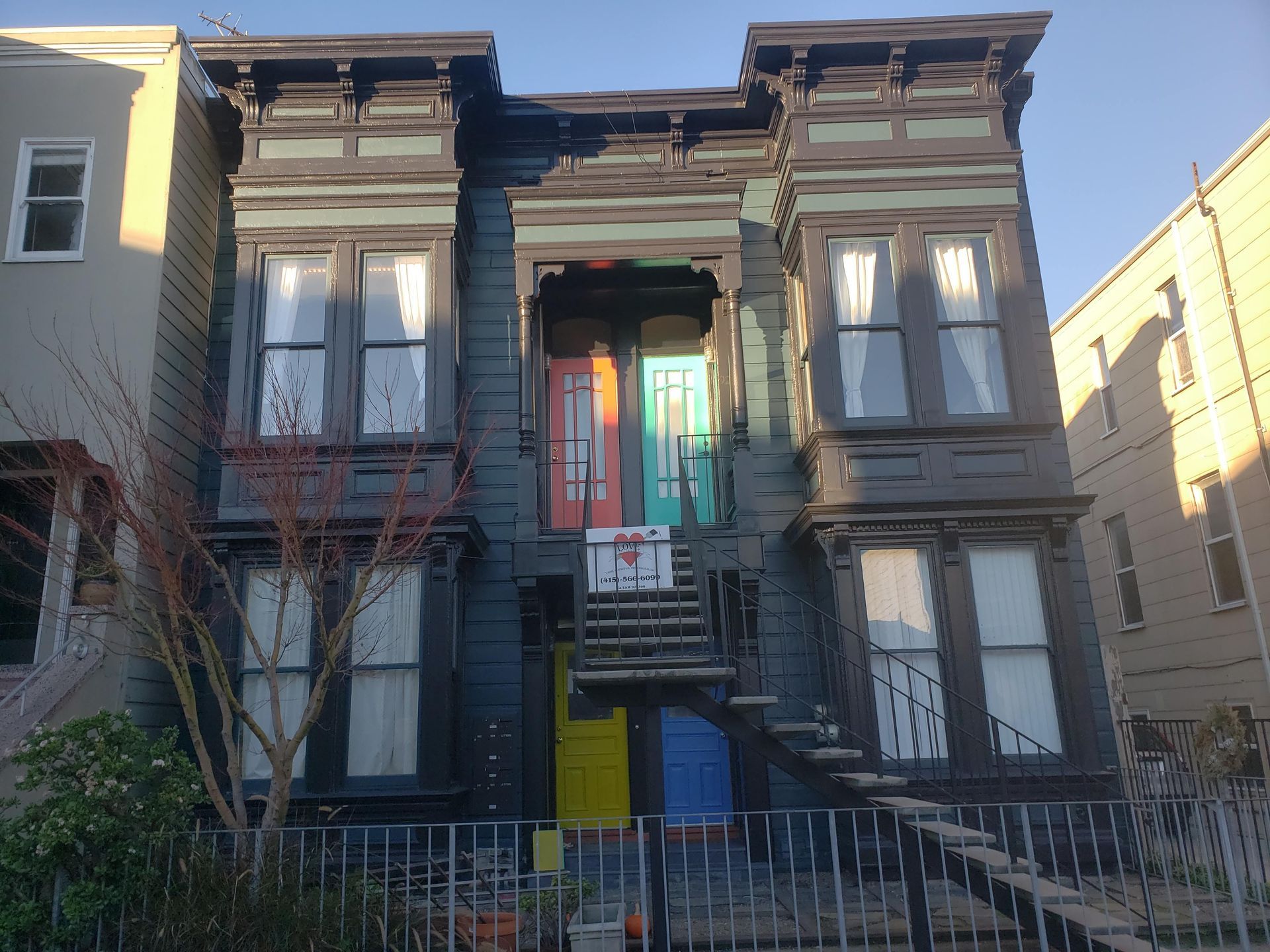 Two-story house with multiple colorful doors, black siding, and exterior stairs.