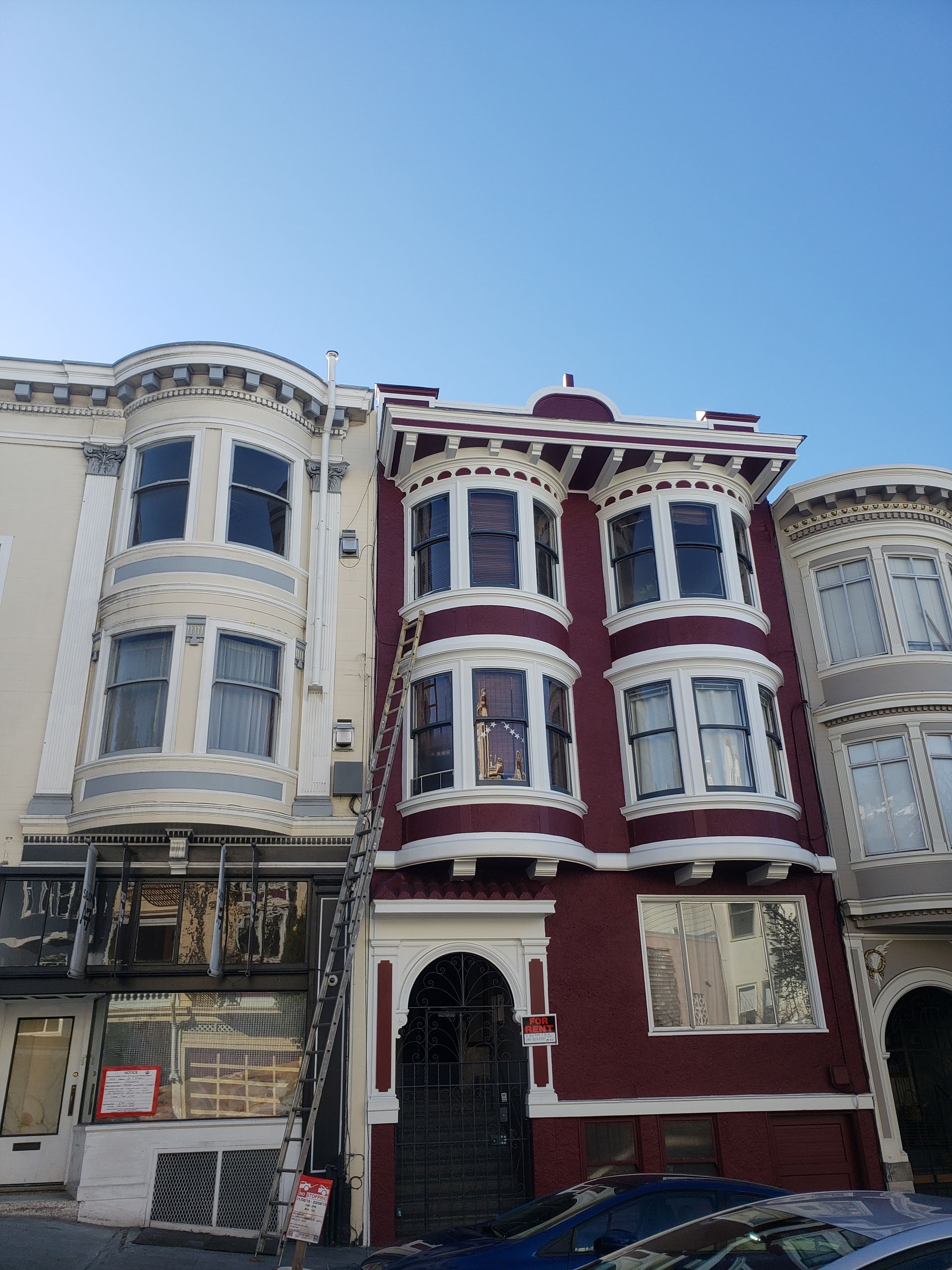 Buildings in San Francisco, one dark red with bay windows, flanked by two other buildings with architectural detail.