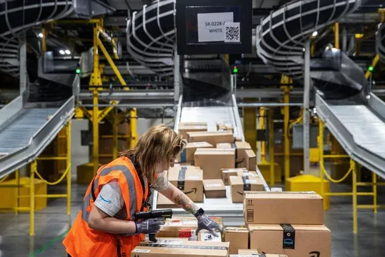 Amazon Warehouse worker scanning packages on a conveyor belt, orange vest, industrial setting.