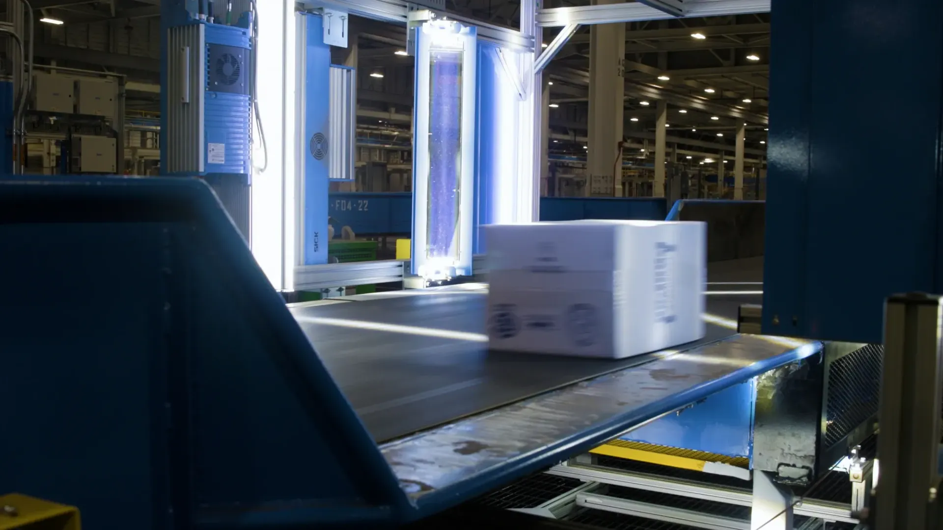 Box on conveyor belt in a blue industrial setting, possibly for sorting or shipping.