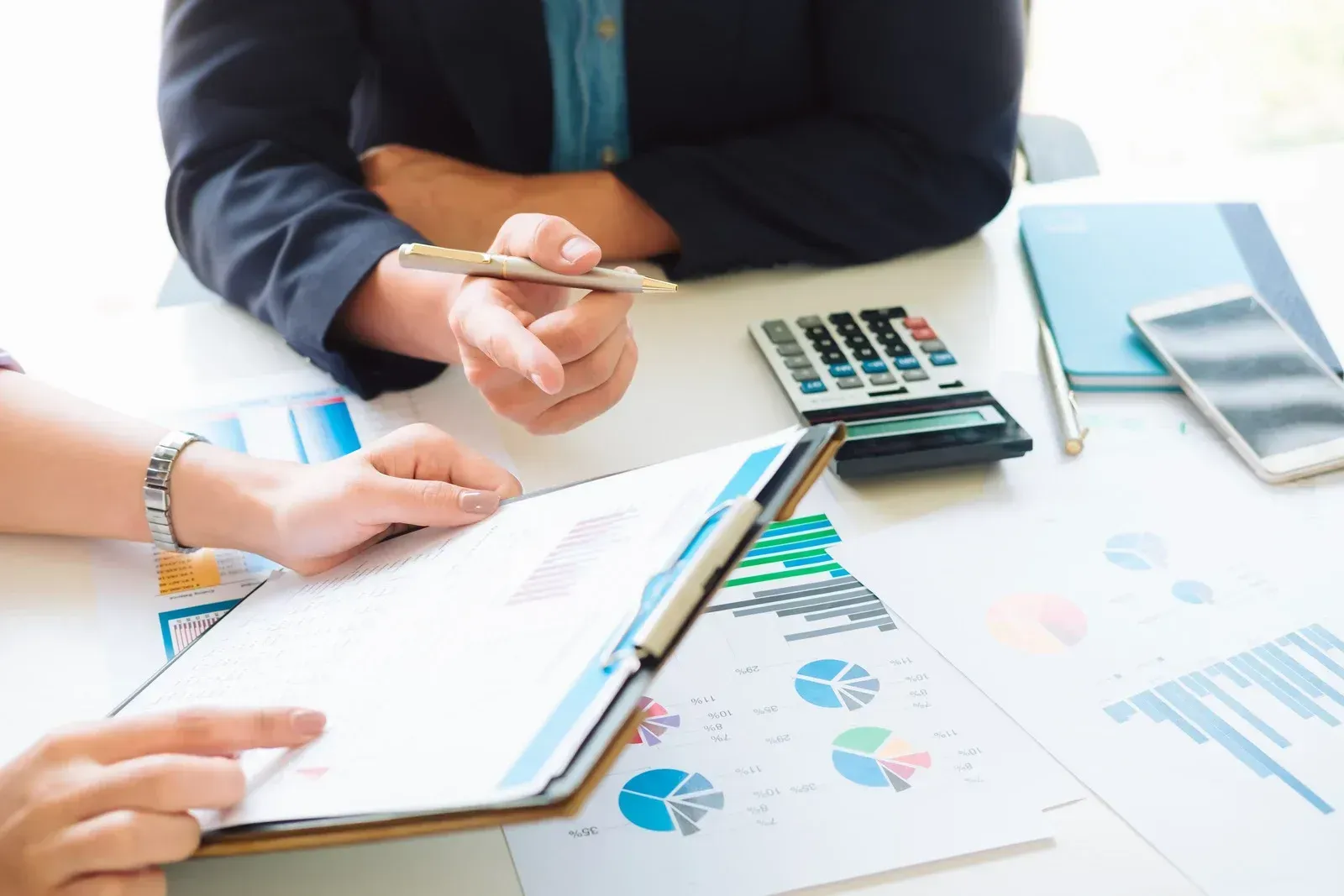 People reviewing financial documents at a desk with charts, calculator, and clipboard
