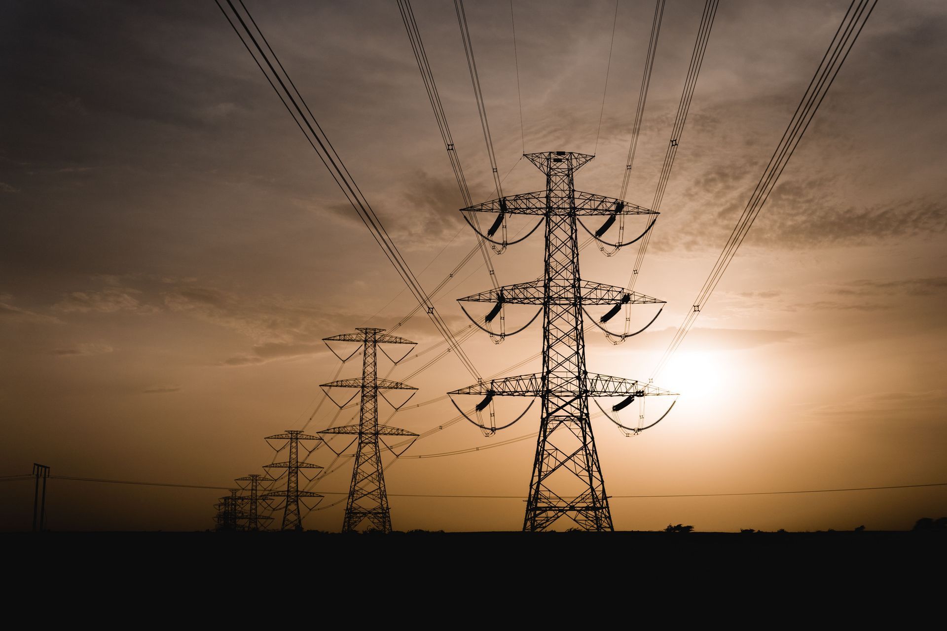 High-voltage power lines silhouetted against a warm sunset sky