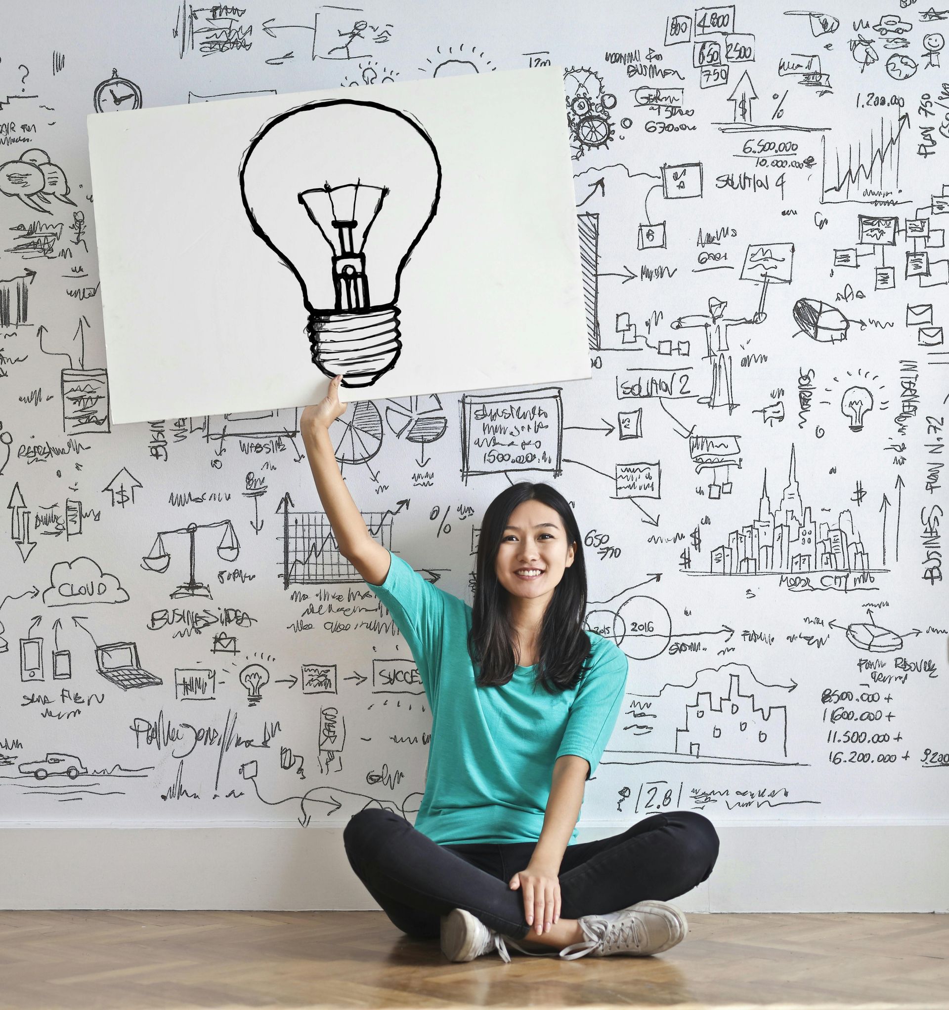 Woman sitting on the floor, holding up a lightbulb drawing in a patterned room.