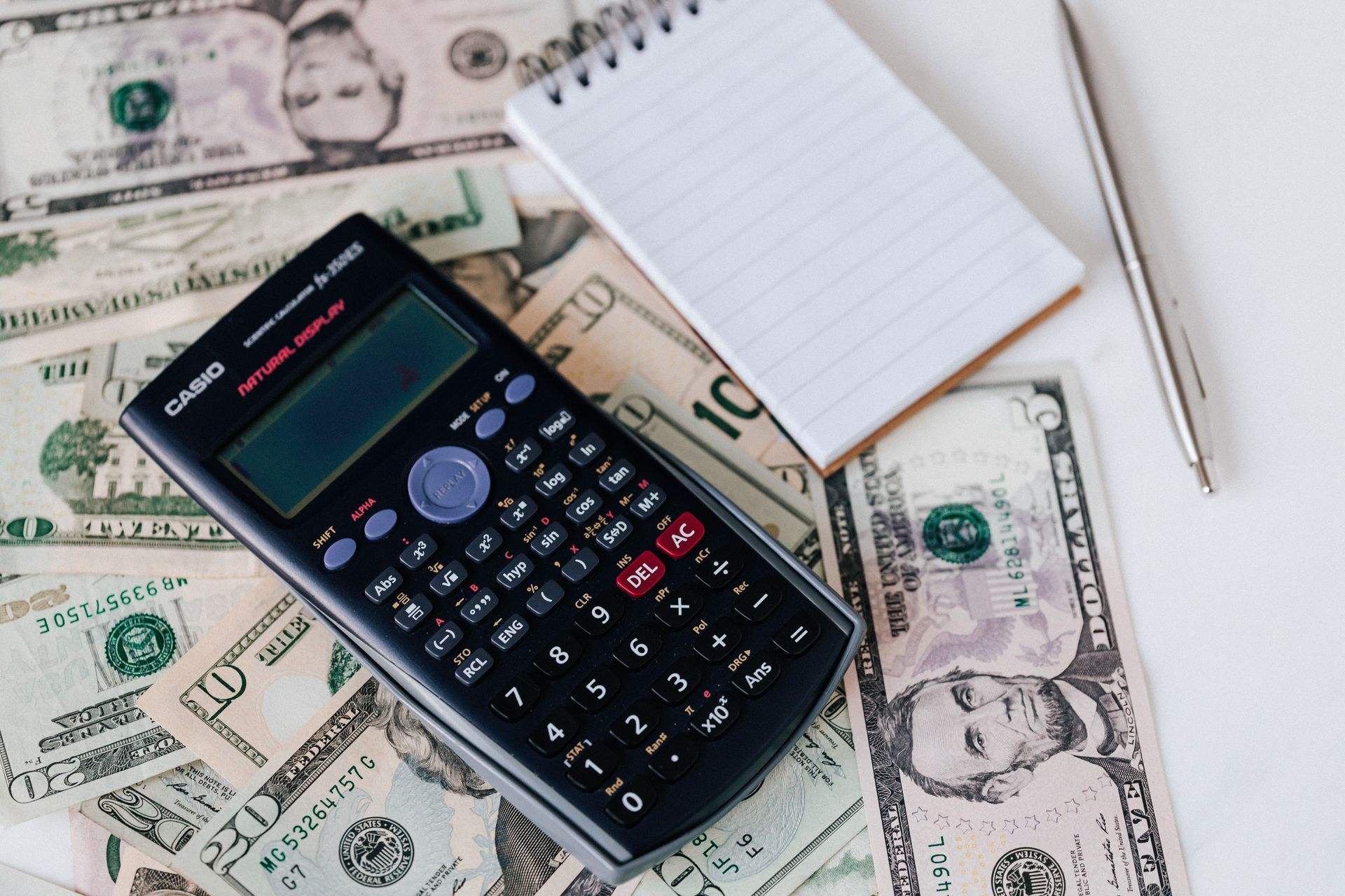 Calculator on U.S. dollar bills beside a notepad and pen, symbolizing budgeting or finance.