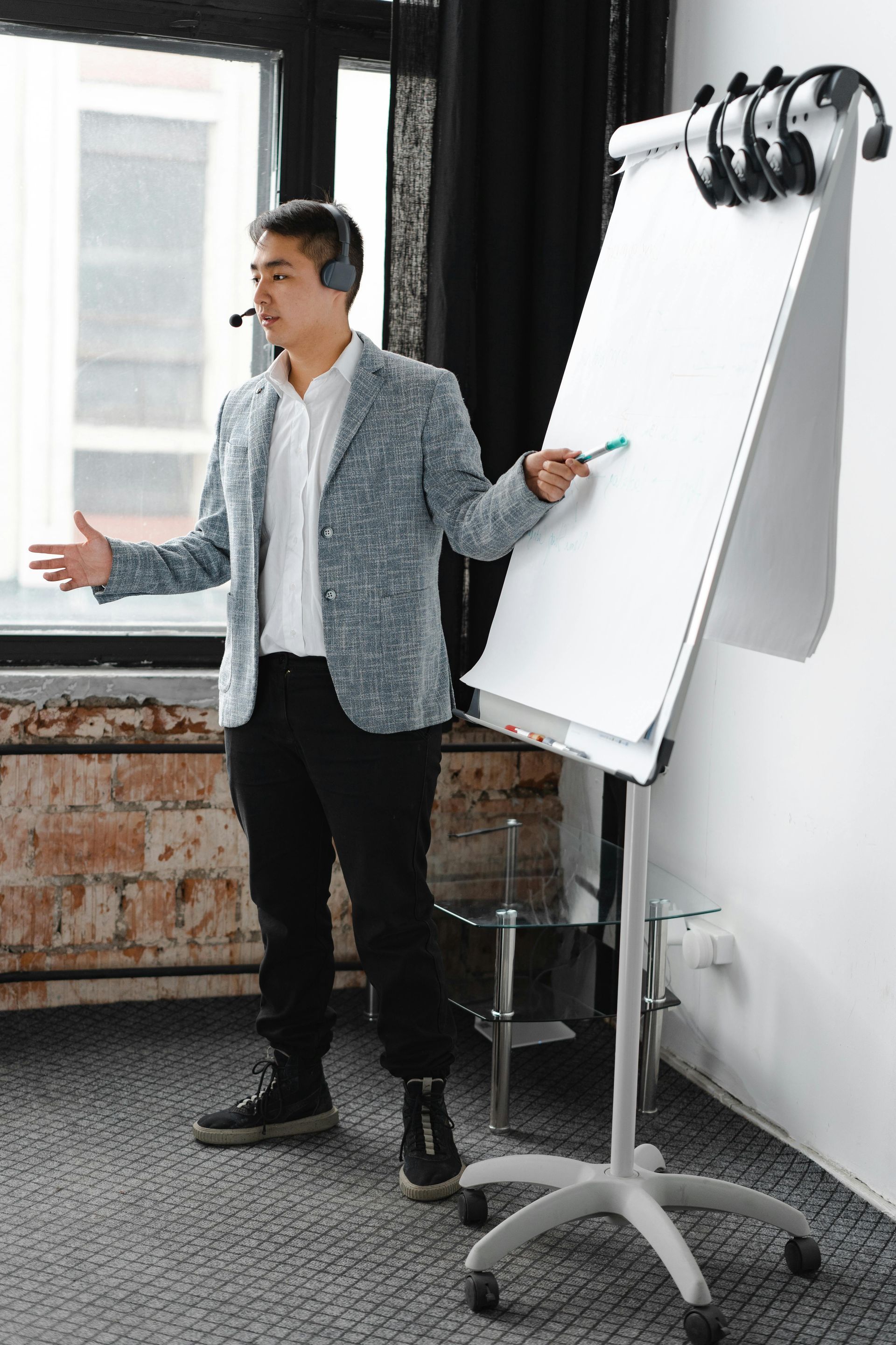 Man speaking beside a blank flip chart in a modern office, gesturing with one hand.