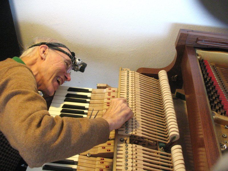 A man wearing glasses is working on a piano