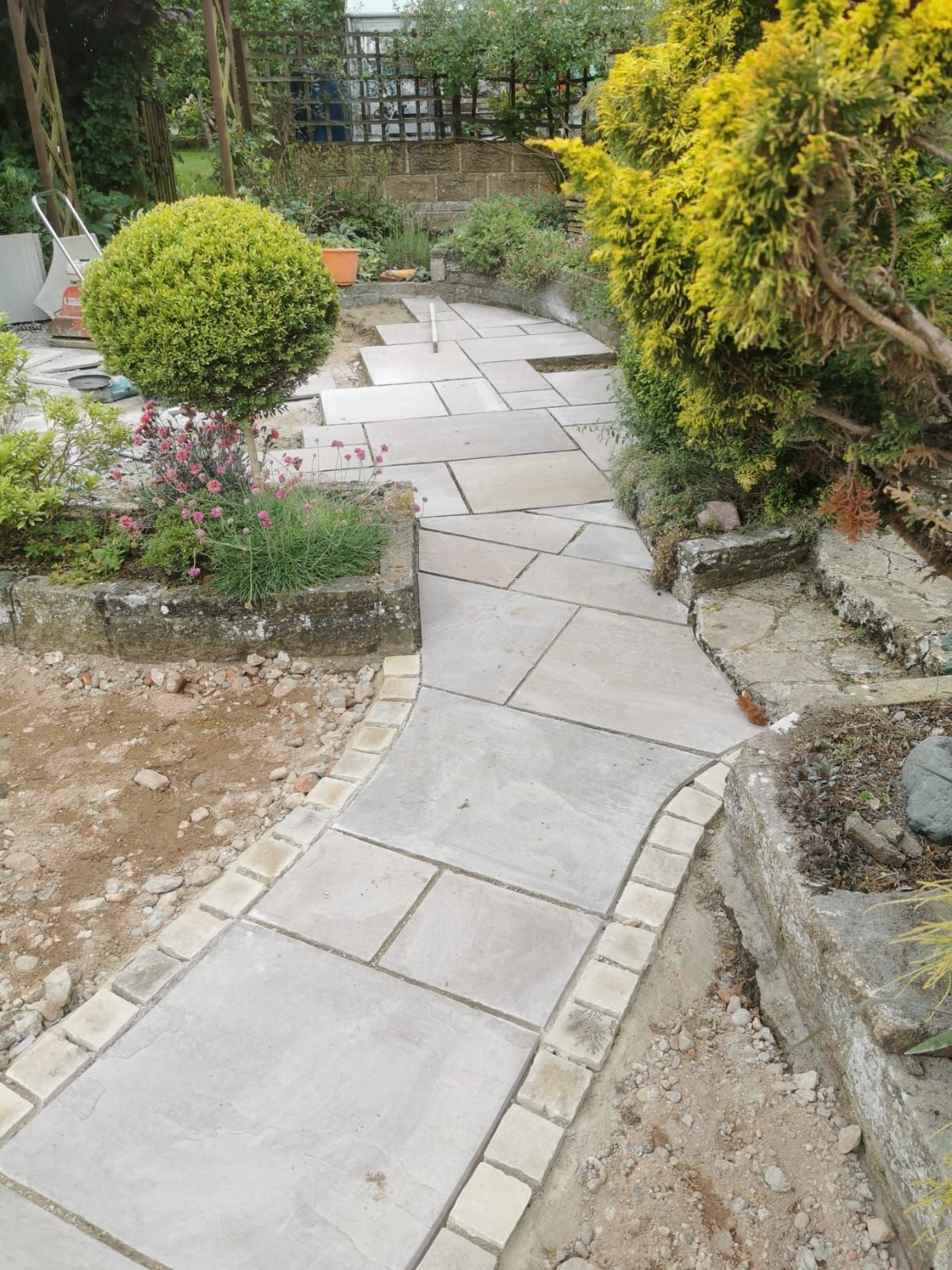 A concrete walkway in a garden surrounded by trees and bushes at Zion Hill Outdoor Spaces, Norfolk