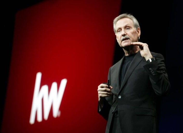 A man in a suit stands in front of a kw logo