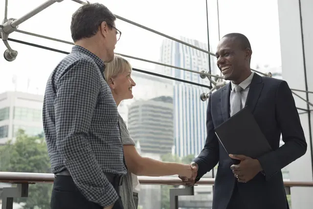 A man and a woman are shaking hands with a man in a suit.