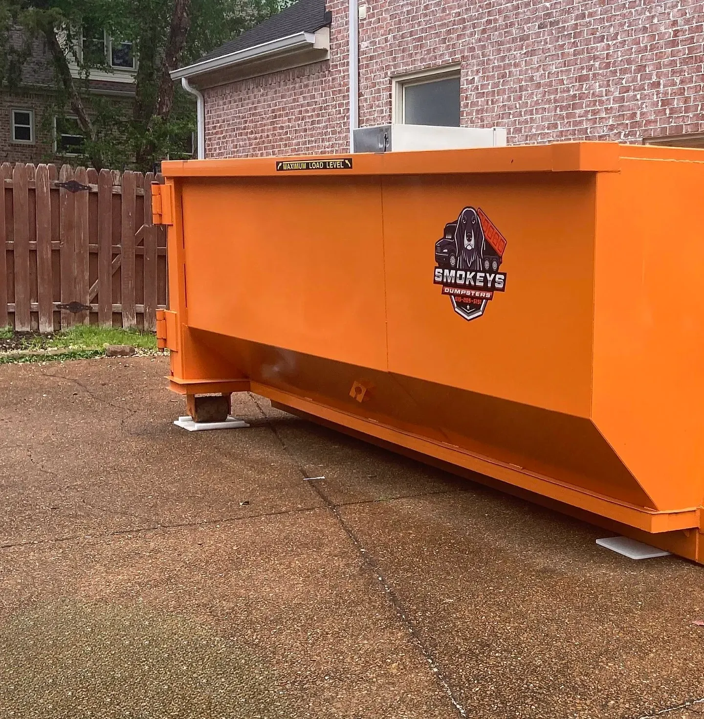 A dumpster is being towed by a dump truck in a driveway.