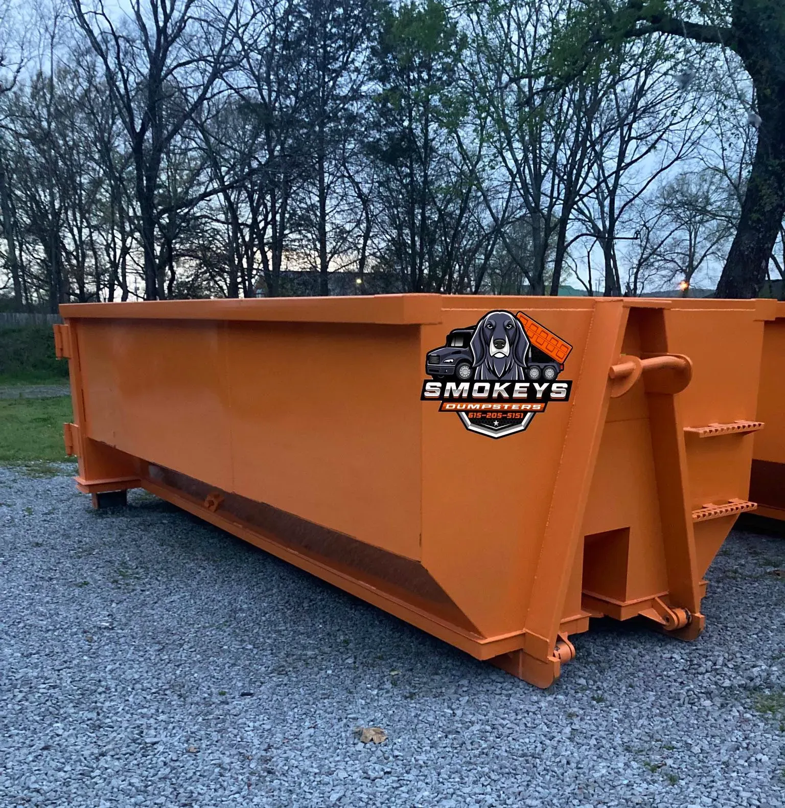 A dumpster is being towed by a dump truck in a driveway.