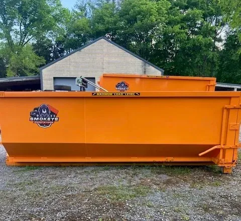 A green dumpster filled with wood is parked in front of a house.