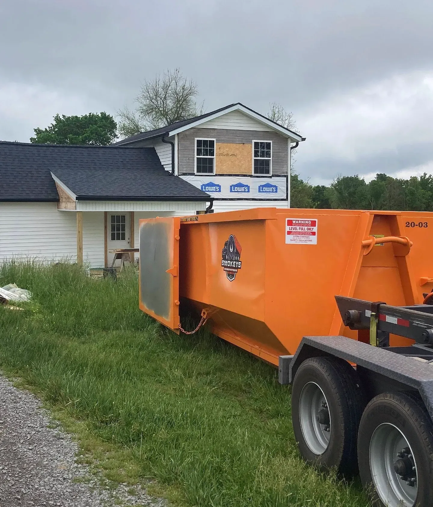 A dumpster is being towed by a dump truck in a driveway.