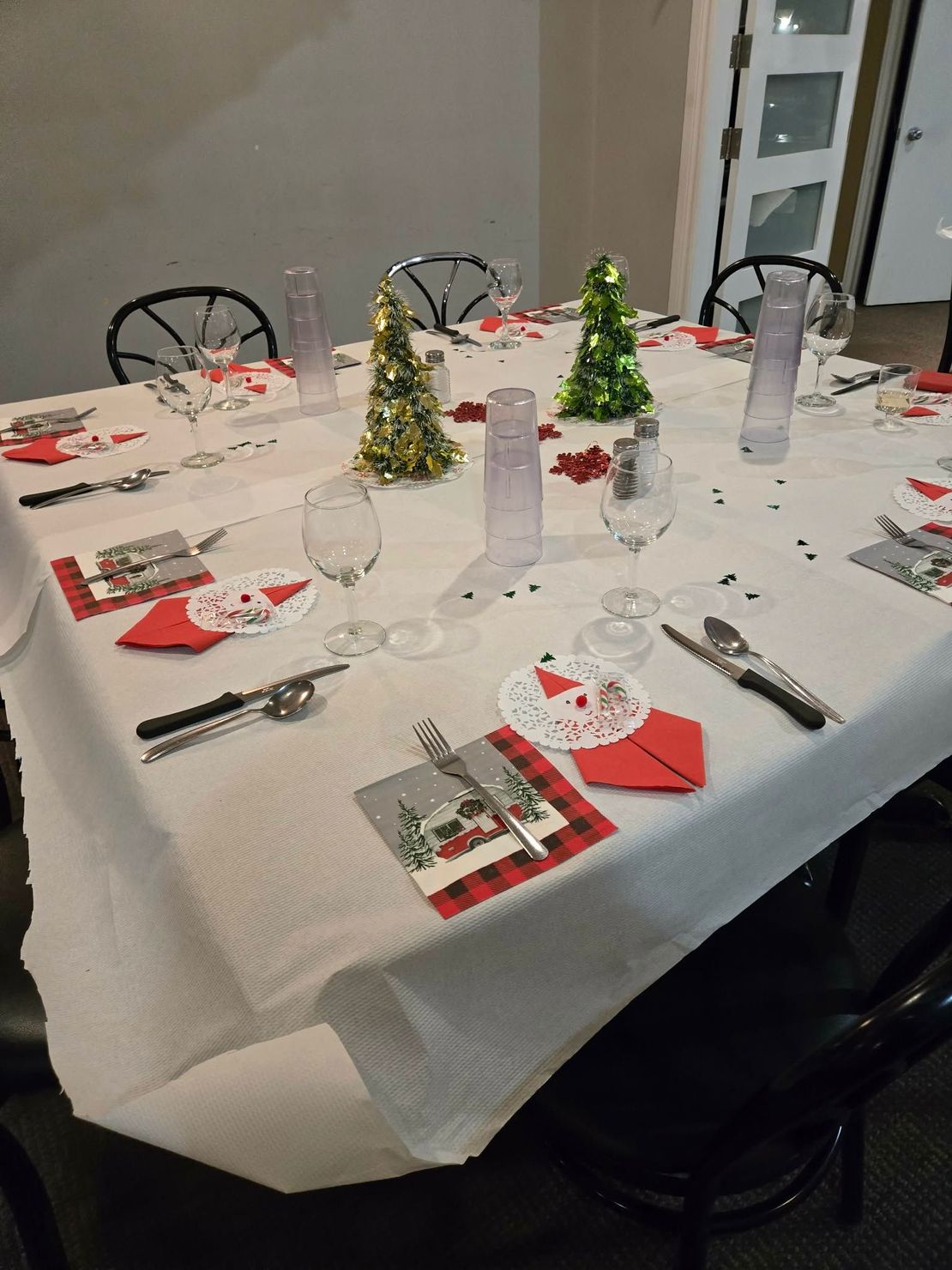 Une table dressée pour un dîner de fête avec des couverts rouges et blancs, des petits sapins de Noël en guirlandes et des verres à pied.