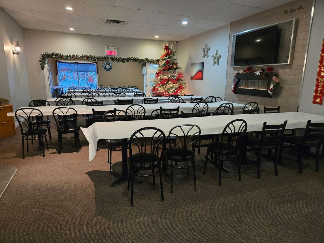 Une salle de banquet aménagée pour une fête de fin d'année, avec des rangées de tables nappées de blanc, des chaises noires et un sapin de Noël décoré.