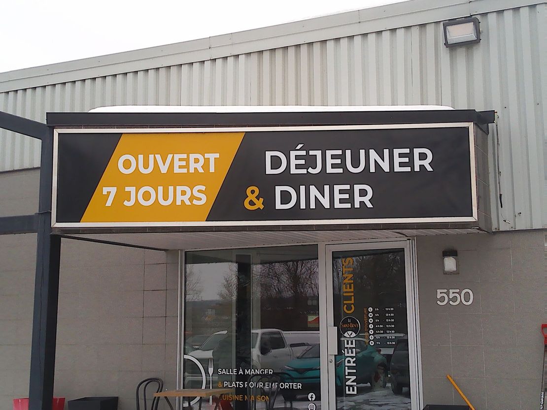 Extérieur d'un restaurant avec une enseigne indiquant « OUVERT 7 JOURS » et « DÉJEUNER & DINER » au-dessus d'une porte d'entrée vitrée.
