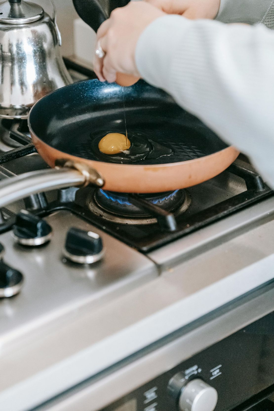 Une personne casse un œuf dans une poêle à frire couleur cuivre sur une plaque de cuisson à gaz.
