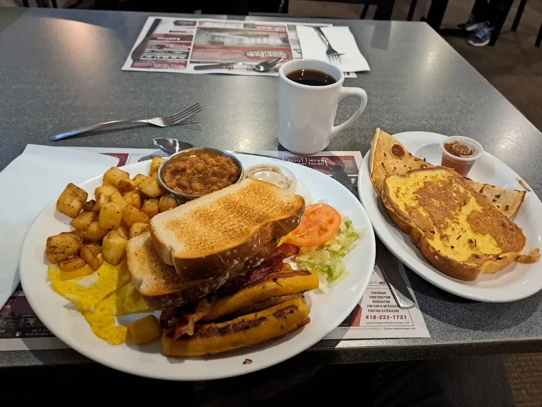 Un petit-déjeuner typique de diner américain, avec du pain grillé, du bacon, des pommes de terre rissolées, une tasse de café et une portion de pain perdu servie à part.