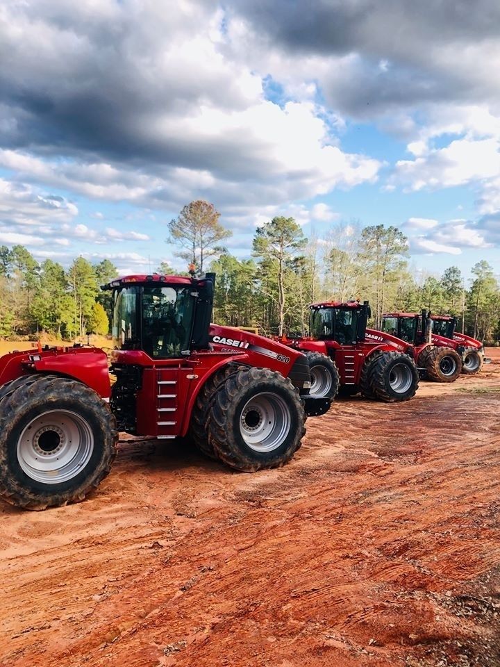 Red tractors lined up on a dirt road under a cloudy sky in a rural field
