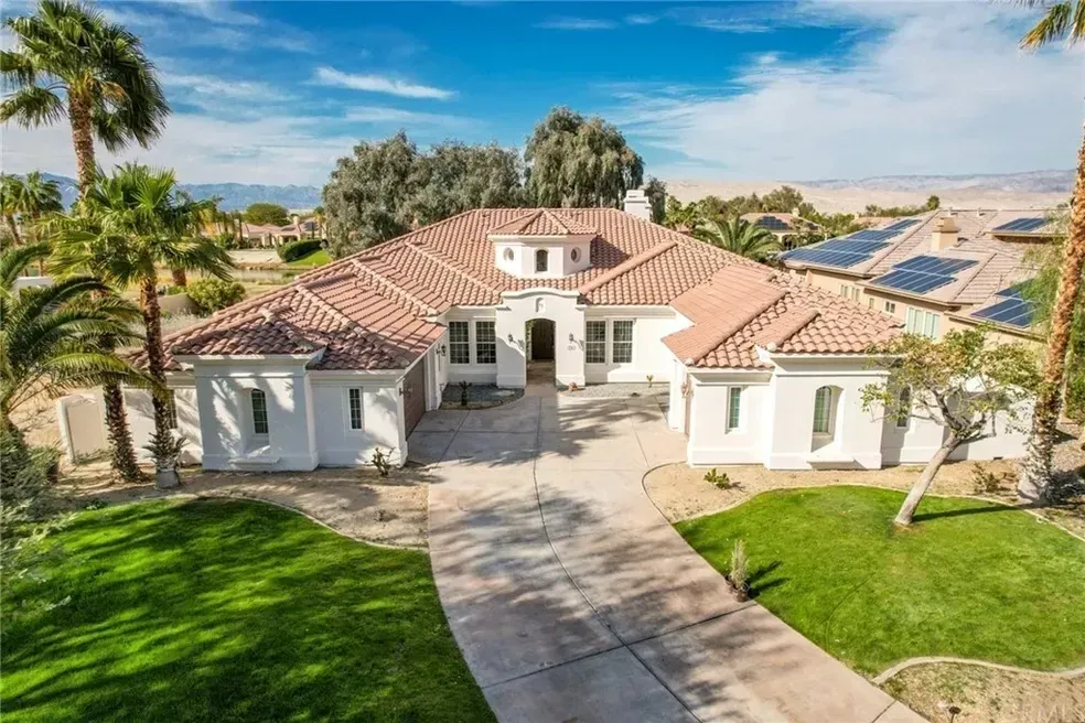 An aerial view of a large white house with a red tile roof surrounded by palm trees.