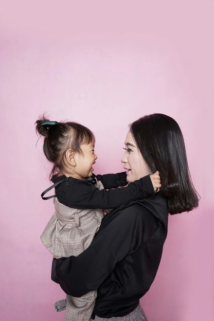 A woman is holding a little girl in her arms on a pink background.