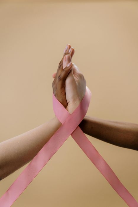 Two people are holding hands with a pink ribbon.