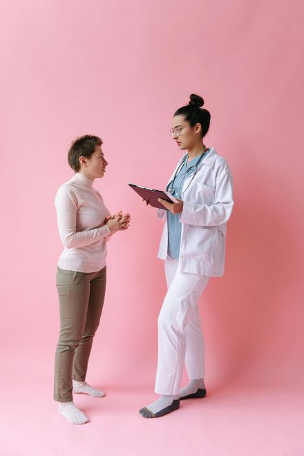 A doctor is talking to a patient on a pink background.