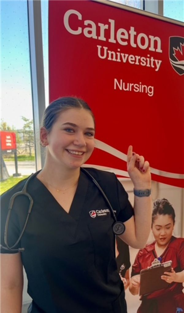 Carleton University Nursing booth with smiling staff member in black scrubs pointing at a red sign