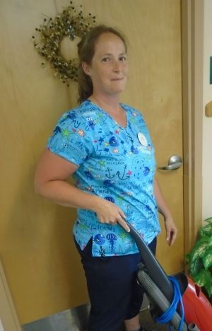 Woman in blue scrubs holding a vacuum cleaner in a hallway by a decorated door