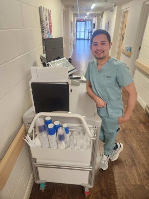 Healthcare worker smiling beside a hospital supply cart in a hallway