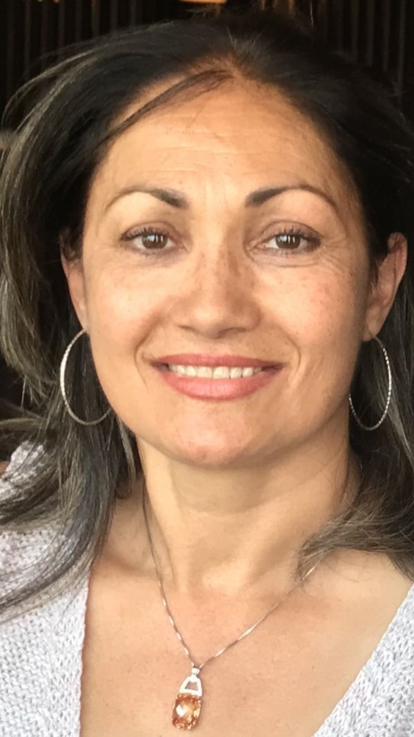 Headshot of a smiling woman with dark hair, hoop earrings, and a necklace on a dark background