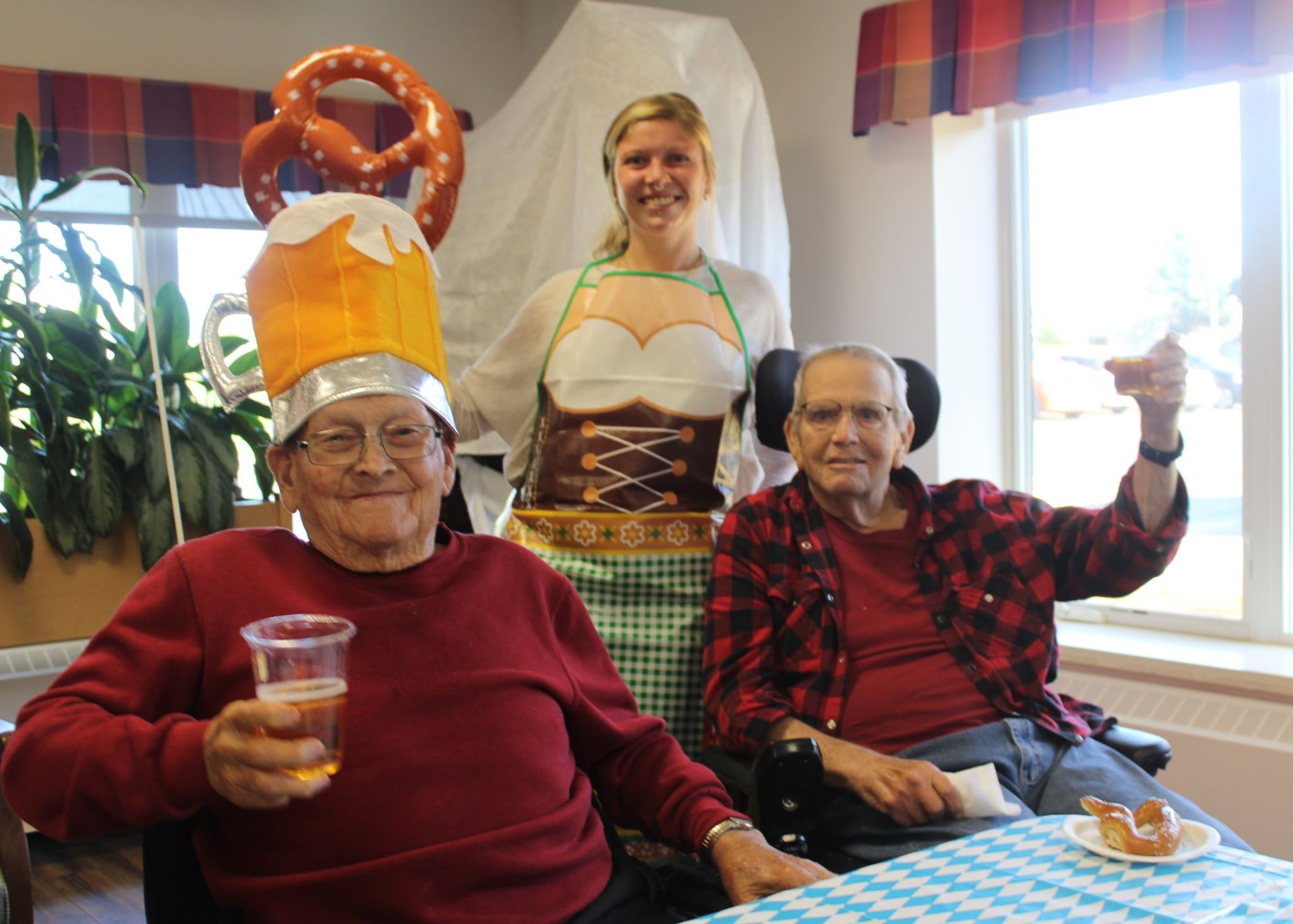 Three people at a festive indoor gathering, smiling with drinks and snacks; one wears a paper hat.